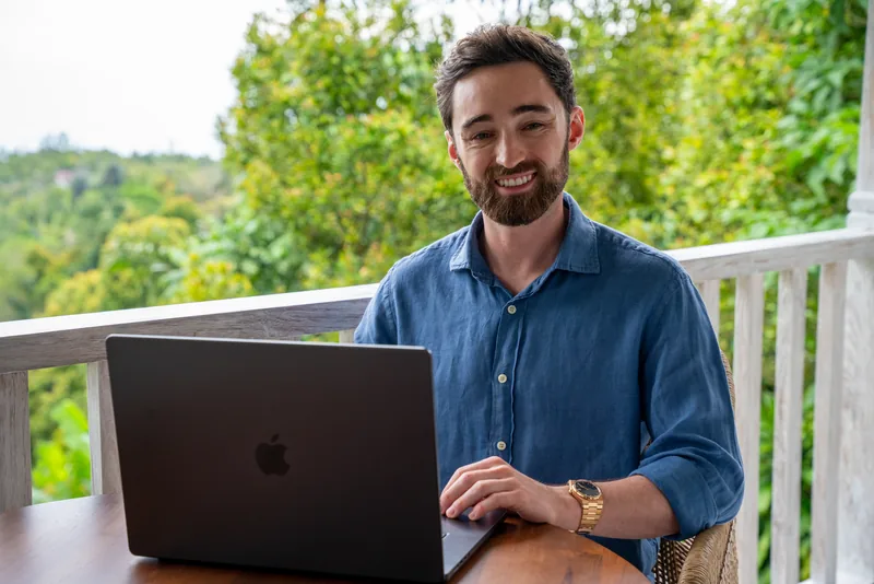 Patrick sonriendo frente a su laptop, trabajando en una terraza
